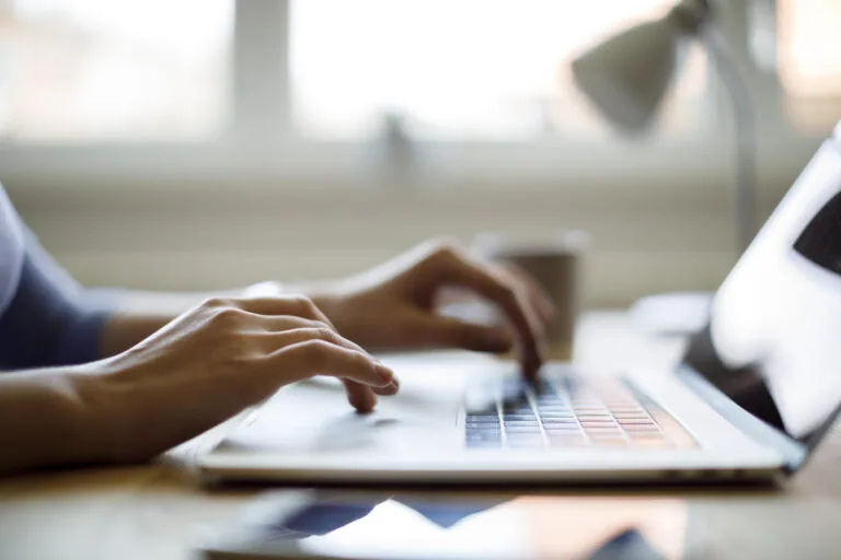 Close up of woman's hands as she types on a laptop and uses the trackpad